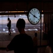 Industrial workers waiting under a large clock symbolising downtime and production delays.